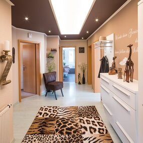 Modern eingerichteter Flur mit afrikanischen Dekofiguren, Tiermusterteppich und Wandkunst.