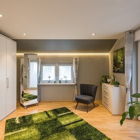 Modern eingerichtetes Schlafzimmer mit Kleiderschrank, Sessel, Pflanzen und großem Fenster.