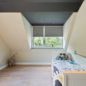 Modernes Kinderzimmer mit Dachschräge, Holzboden, Fenster und gemütlichem Bett mit Kuscheltieren.