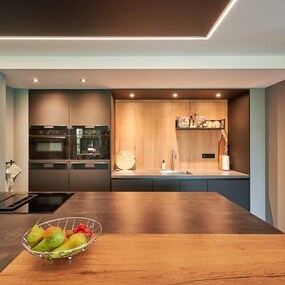 Moderne Küche mit Kochinsel, dunklen Fronten, Einbaugeräten und stilvoller Beleuchtung.